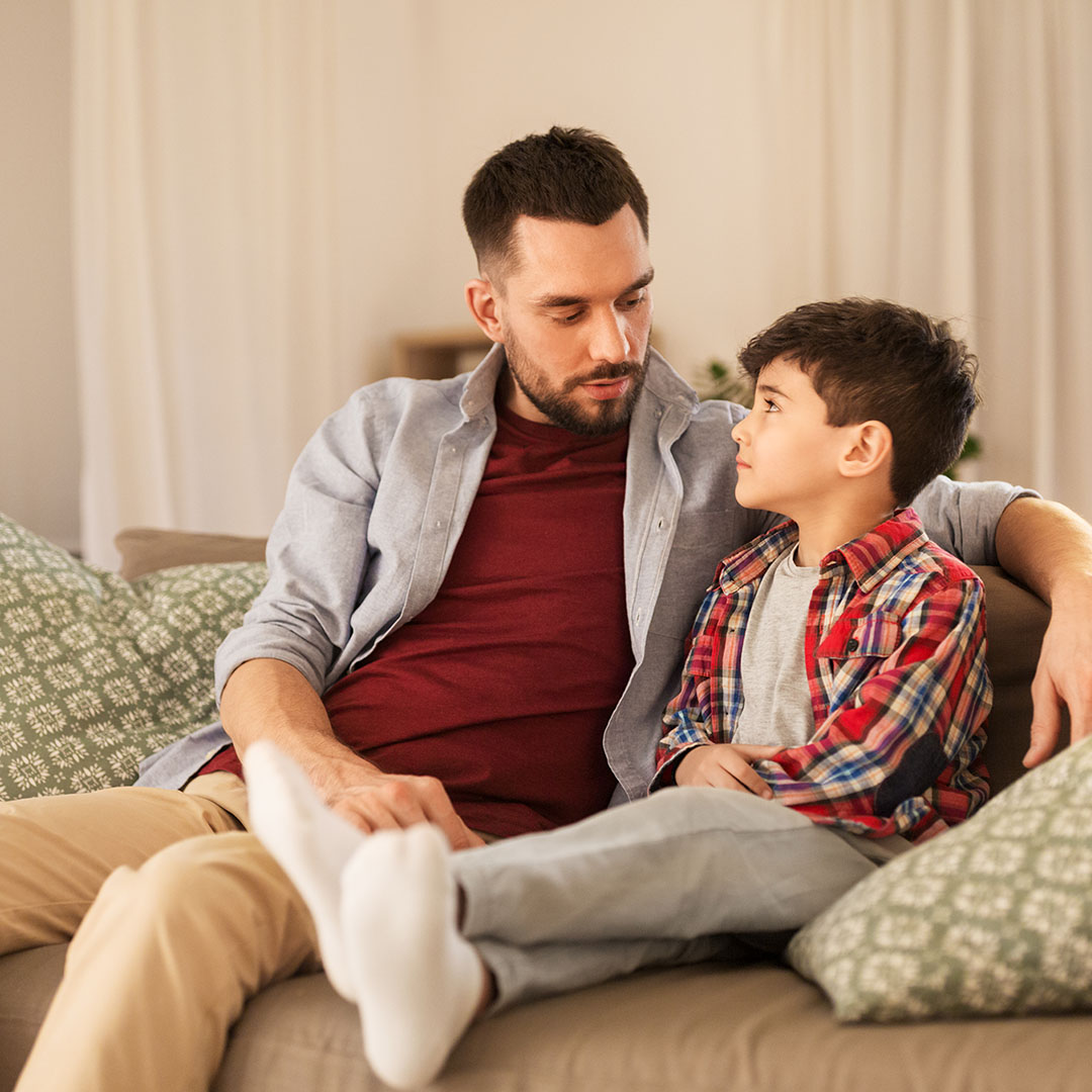 foster dad talking to young boy on couch